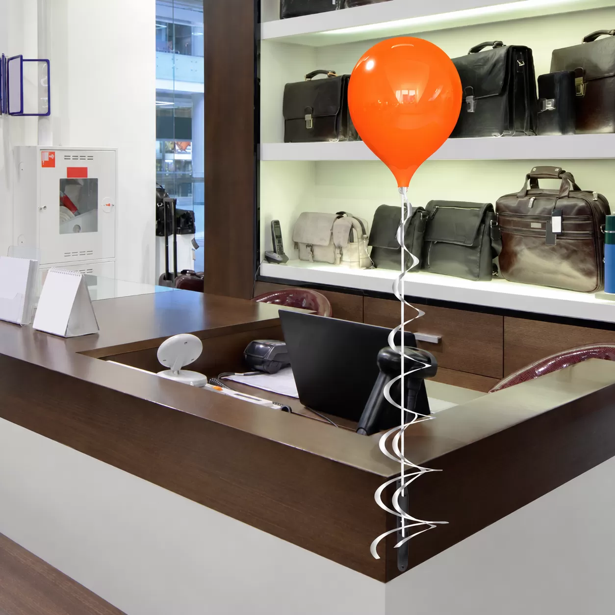 Orange PermaShine balloon on a white stem and vertical bracket at a retail counter