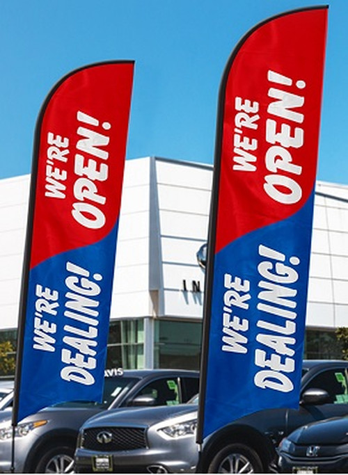 Red and blue We Are Open We Are Dealing flags displayed outside a dealership