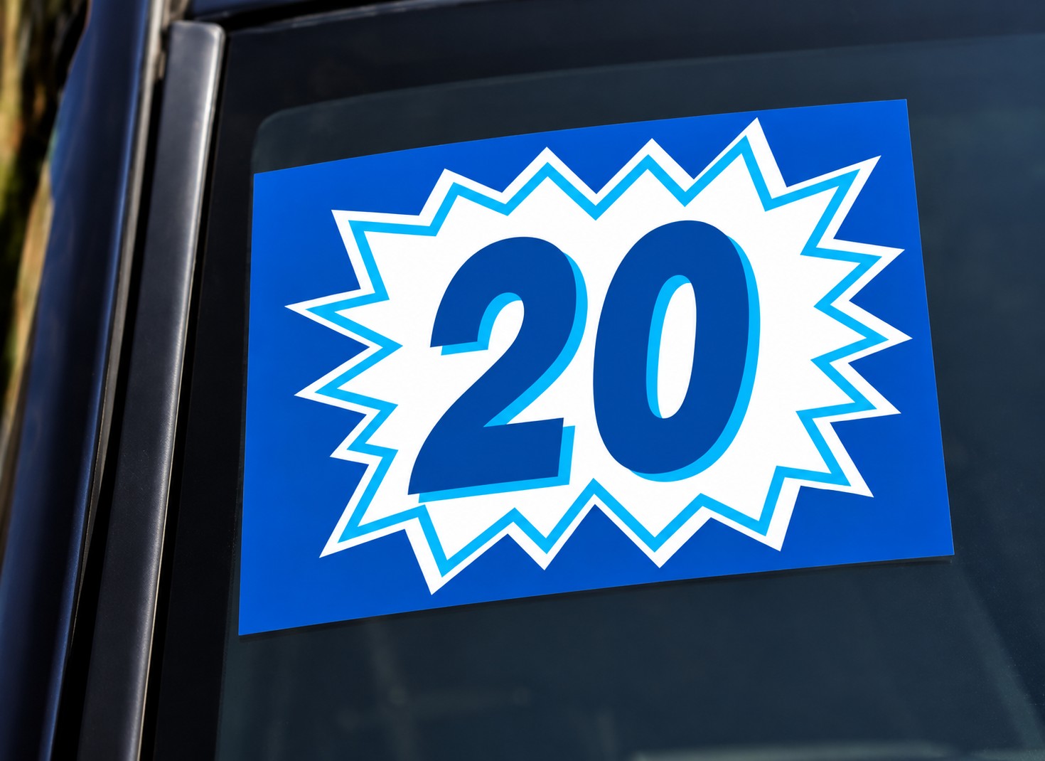Blue and white burst model-year sticker showing 20 on a vehicle windshield