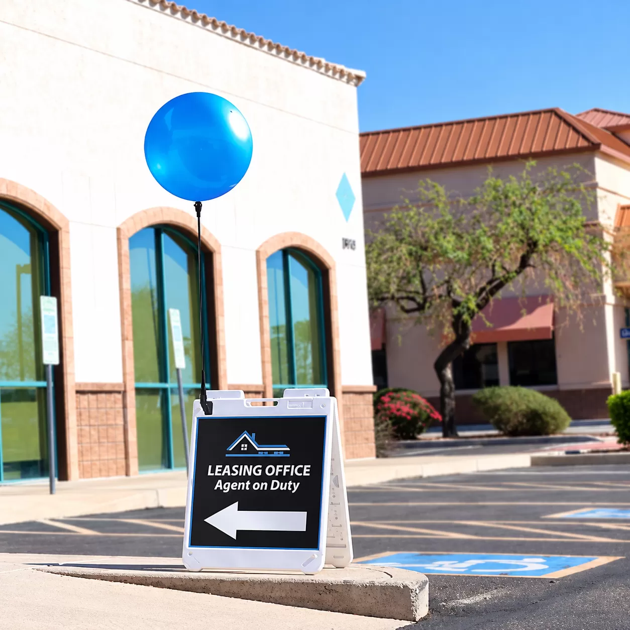 Blue DuraBalloon mounted above an A-frame leasing office sign